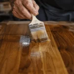 How to Apply Polyurethane to Wood for a Smooth Finish Hands using a bristle brush to apply polyurethane to a wood tabletop